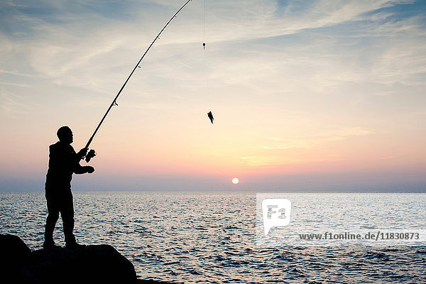 Silhouette eines Mannes  der bei Sonnenuntergang fischt