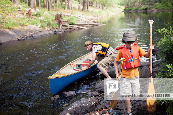 Father and son pushing canoe in river