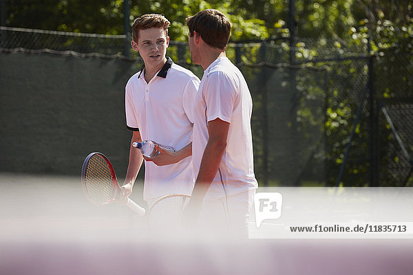 Tennisspieler mit Tennisschlägern im Gespräch auf dem sonnigen Tennisplatz