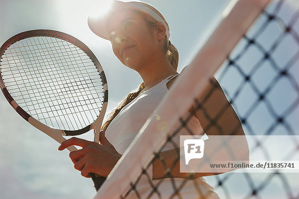 Selbstbewusste junge Tennisspielerin mit Tennisschläger am Netz