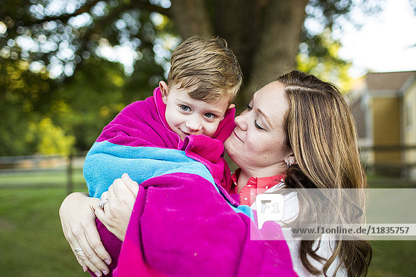 Liebevolle Mutter hält den Sohn in ein Handtuch gewickelt im Sommerhof.