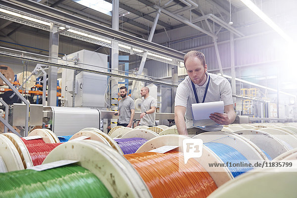 Male worker with clipboard checking multicolor spools in fiber optics factory
