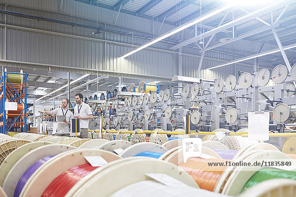 Male supervisor and worker checking inventory behind multicolor spools in fiber optics factory