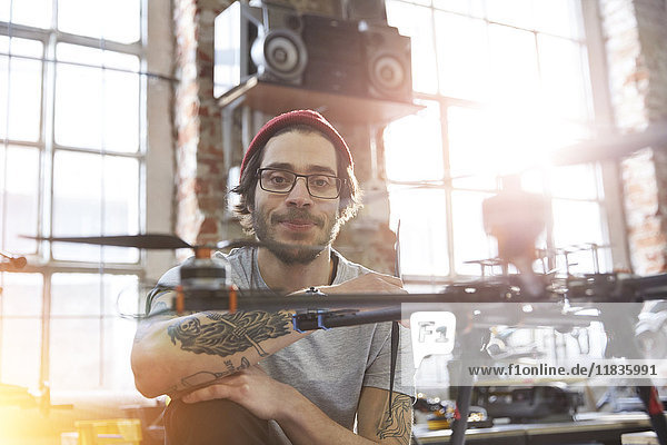 Portrait confident male designer with tattoos working on drone in workshop