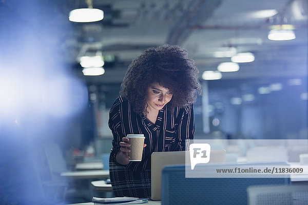 Geschäftsfrau arbeitet spät am Laptop  trinkt Kaffee im dunklen Büro