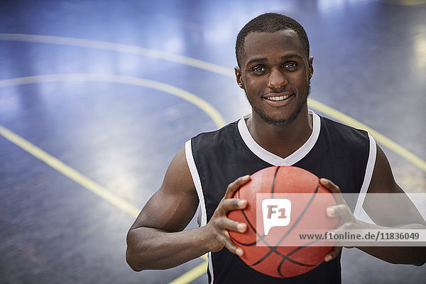 Portrait smiling young male basketball player holding basketball on court