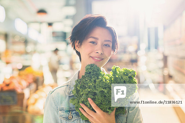 Portrait smiling young woman holding fresh kale in grocery store market