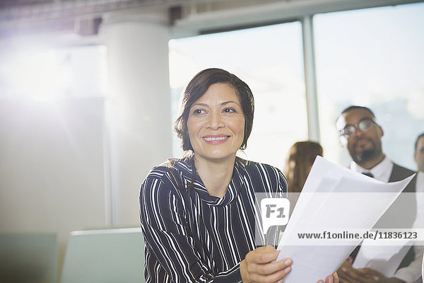 Lächelnde Geschäftsfrau mit Papierkram in Konferenzraumbesprechung