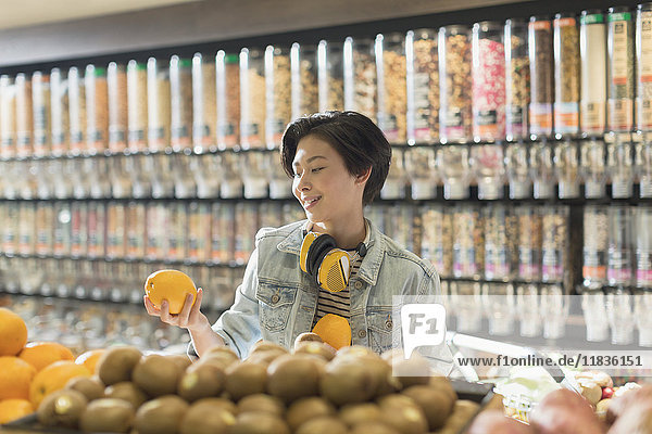 Junge Frau mit Kopfhörern beim Lebensmitteleinkauf  hält eine Orange auf dem Markt