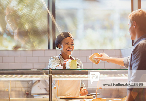 Lächelnde Mitarbeiterin  die einen Kunden an der Käsetheke eines Lebensmittelmarktes bedient