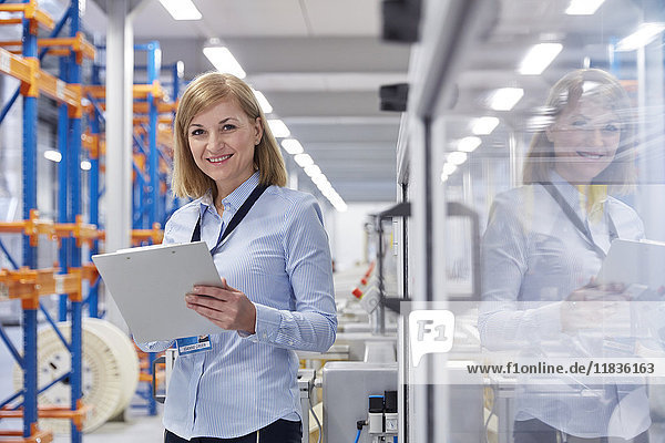 Portrait smiling female supervisor with clipboard in fiber optics factory
