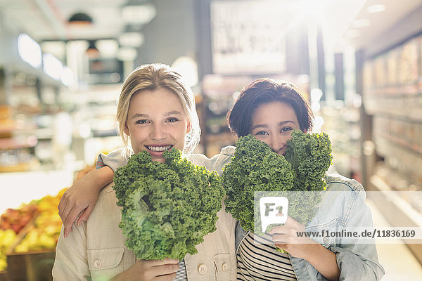 Portrait playful young lesbian couple holding fresh kale in grocery store market