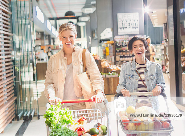 Smiling young women pushing shopping carts in grocery store market