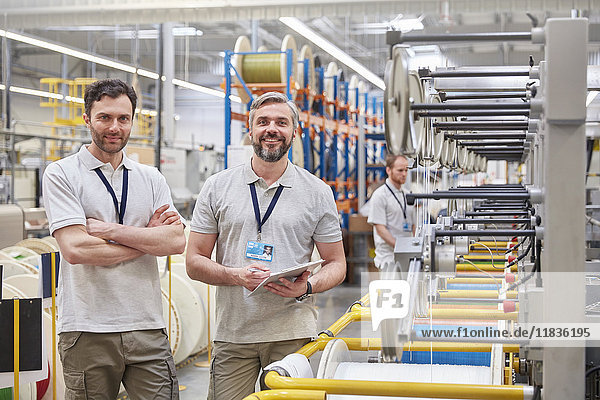 Portrait smiling  confident male workers with digital tablet on fiber optics factory floor