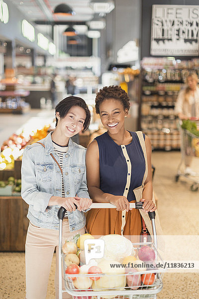 Porträt lächelnd junge lesbische Paar mit Einkaufswagen Lebensmittelgeschäft Einkaufen in Markt