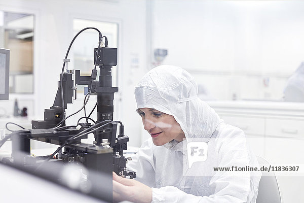 Female engineer in clean suit using equipment in fiber optics research and testing laboratory