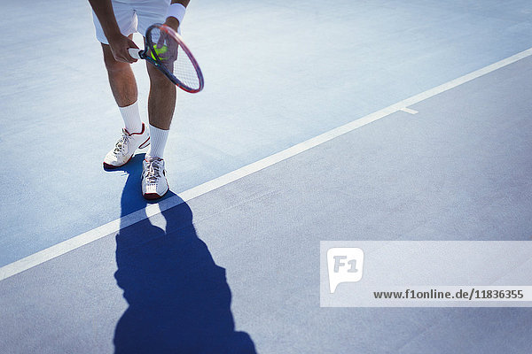 Junger männlicher Tennisspieler,  der sich darauf vorbereitet,  den Ball auf dem sonnigen blauen Tennisplatz zu servieren.