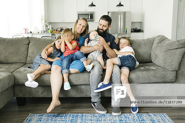 Family with four children (6-11 months  2-3  6-7) spending time on sofa
