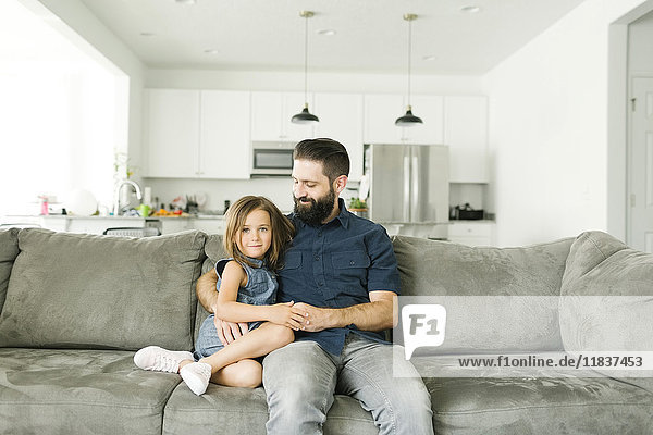 Father with daughter (6-7) sitting on sofa in living room