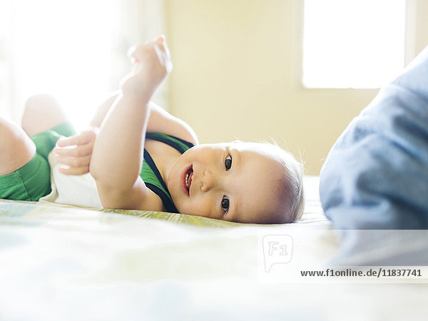 Porträt eines kleinen Jungen (12-17 Monate)  der auf dem Bett liegt und in die Kamera schaut