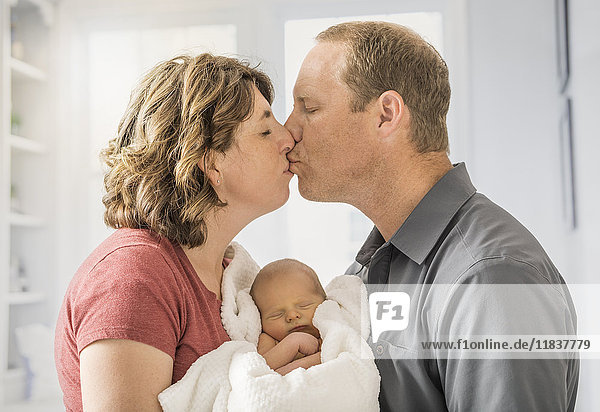 Eltern halten ihren kleinen Sohn (0-1 Monate) und küssen sich