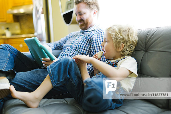 Junge (4-5) und Mann mit digitalem Tablet auf dem Sofa im Wohnzimmer