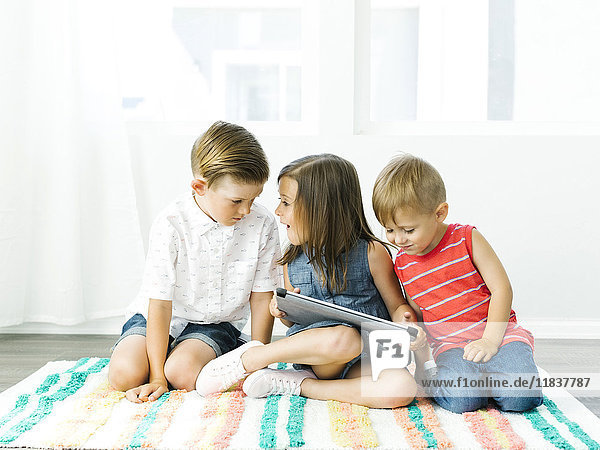 Kinder (2-3  6-7) sitzen auf einem Teppich mit einem digitalen Tablet
