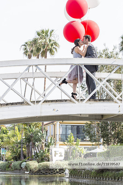Küssendes Paar  das auf einer Brücke mit Luftballons feiert