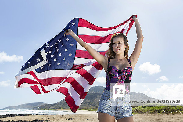 Mixed Race woman holding American flag on beach