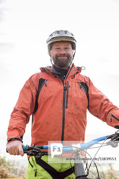 Portrait of smiling Caucasian man splattered in mud holding bicycle