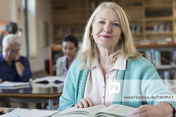 Lächelnde ältere Frau  die in einer Bibliothek ein Buch liest