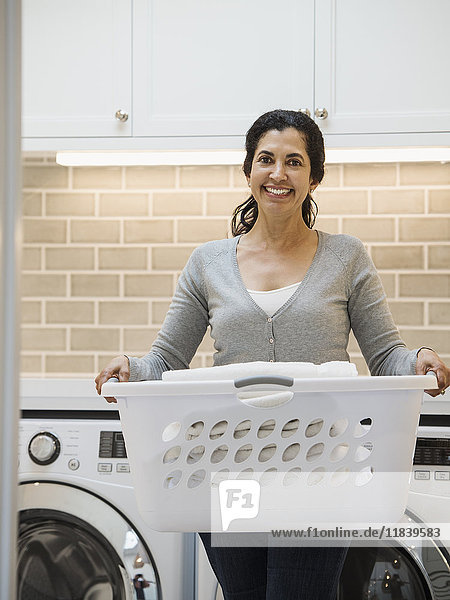 Hispanische Frau trägt Korb in moderner Waschküche