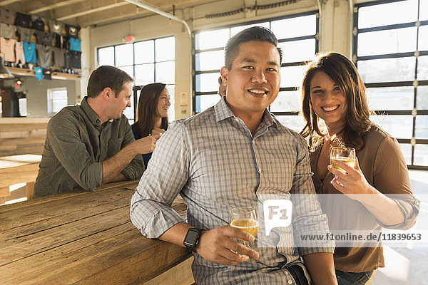 Porträt eines lächelnden Paares  das mit Freunden in einer Brauereikneipe Bier trinkt