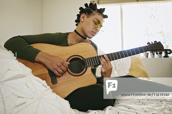 Mixed Race Frau sitzt auf dem Bett und spielt Gitarre