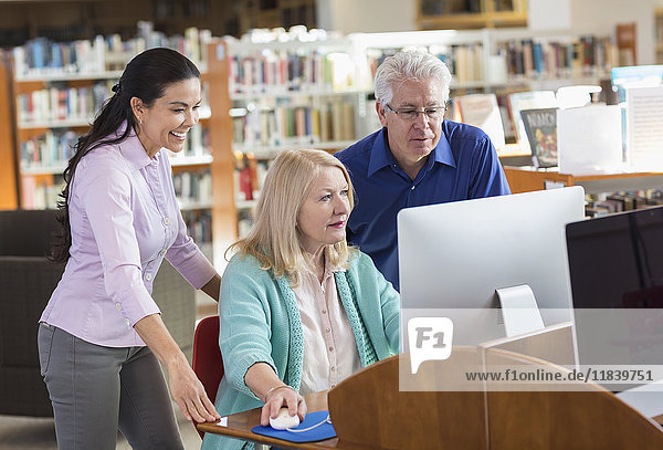 Älterer Mann und Frau benutzen Computer in einer Bibliothek