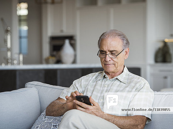Kaukasischer Mann sitzt auf dem Sofa und schreibt eine SMS mit seinem Handy