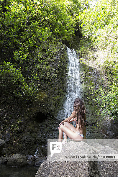 Kaukasische Frau sitzt auf einem Felsen in der Nähe eines Wasserfalls