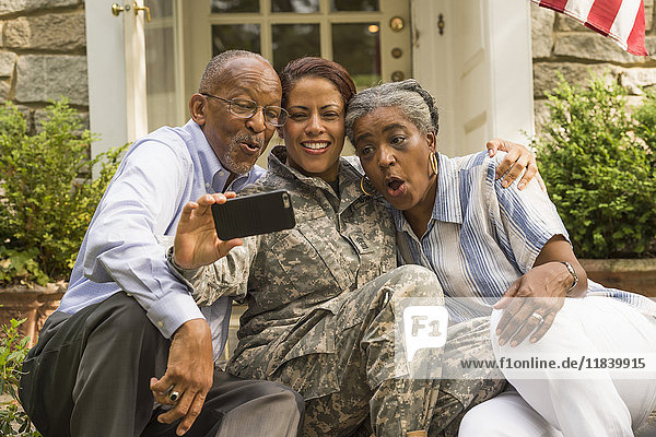 Soldier sitting on front stoop with parents and posing for cell phone selfie