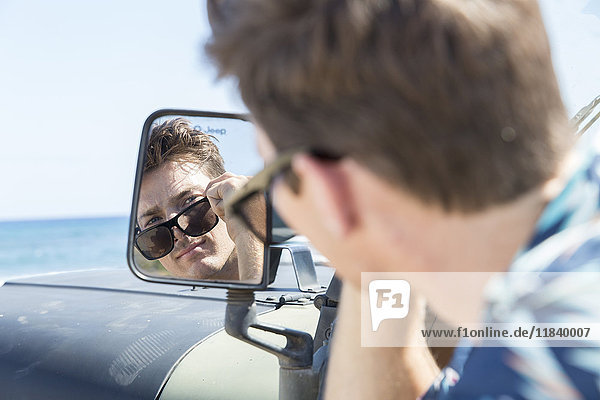 Spiegelung eines kaukasischen Mannes im Seitenspiegel eines Autos am Strand