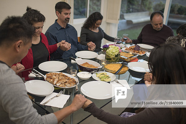 Multi-generation family praying before eating meal