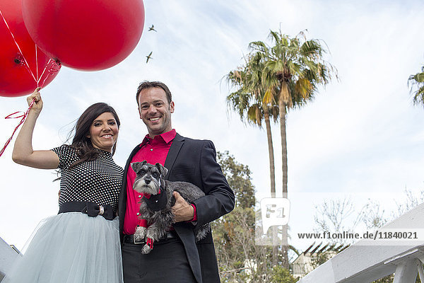 Lächelndes Paar mit Hund und roten Luftballons