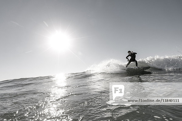 Distant Caucasian man surfing in sunny ocean