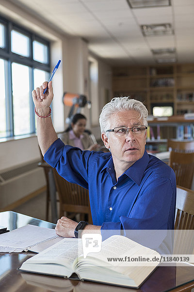 Älterer Mann in der Bibliothek hebt die Hand und stellt eine Frage