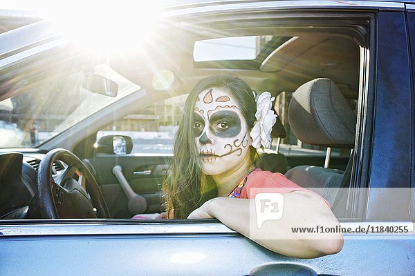 Hispanische Frau fährt Auto und trägt Totenkopf-Gesichtsbemalung