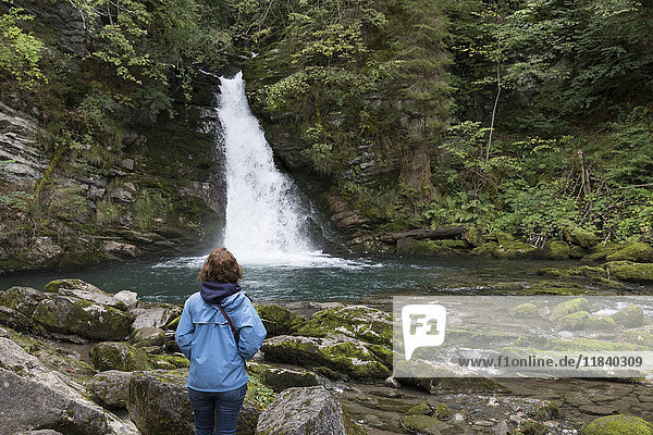 Kaukasische Frau bewundert einen entfernten Wasserfall