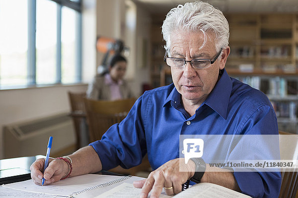 Hispanic man reading book and writing notes in library