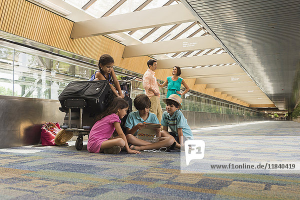 Kinder  die mit ihrer Familie auf dem Flughafen warten und ein digitales Tablet benutzen
