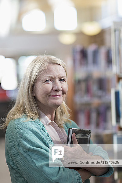 Lächelnde kaukasische Frau mit Buch in der Bibliothek