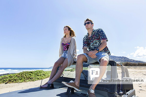Couple sitting on windshield of convertible car on beach