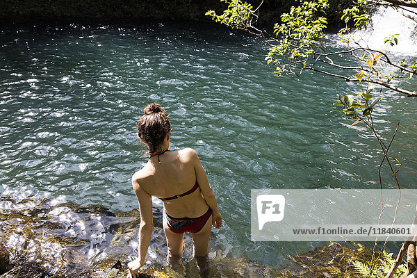 Kaukasische Frau watet im Pool in der Nähe eines Wasserfalls